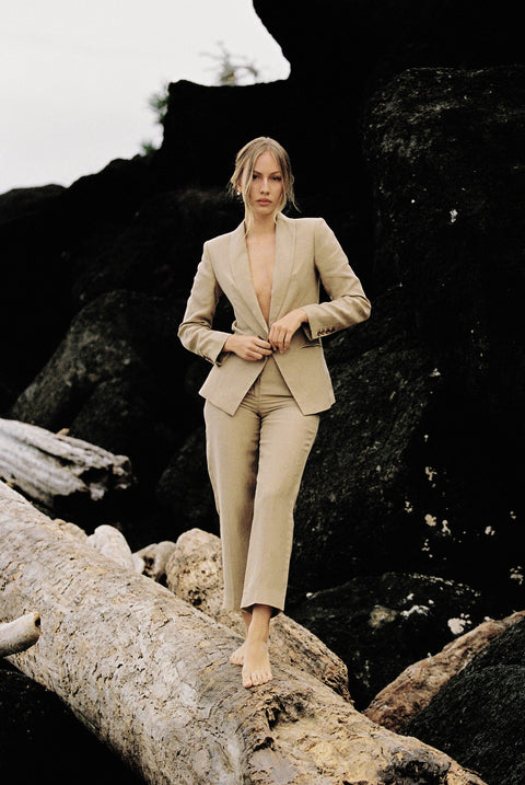 Model wearing a taupe linen blazer and trouser posing on a log by the beach