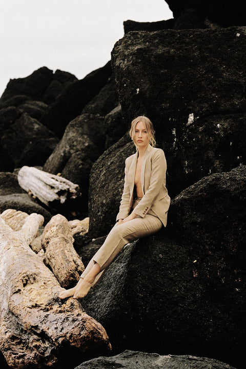 Model wearing a taupe linen blazer and trouser posing on a rock by the beach