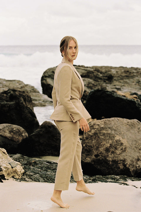 Model wearing a taupe linen blazer and trouser posing by the beach