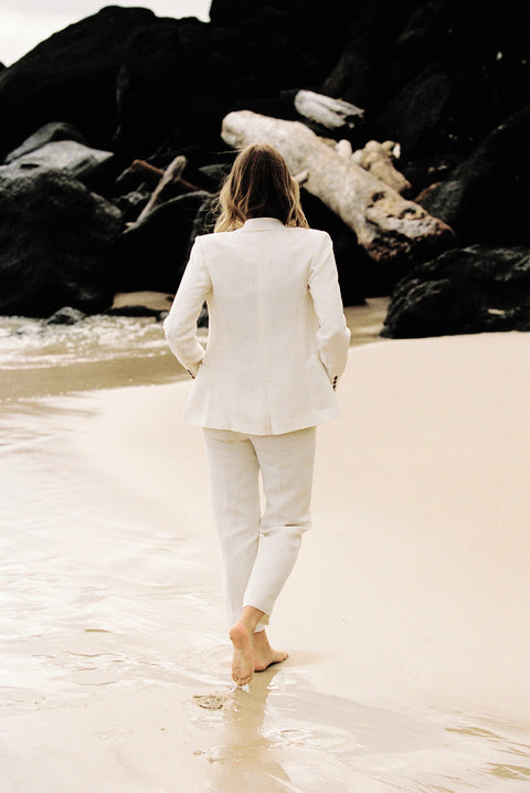 Back view of model wearing a white linen suit by the beach