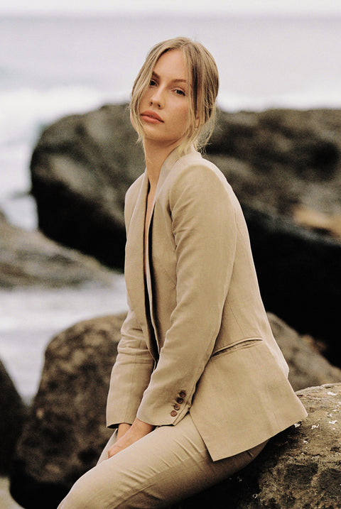 Model wearing a taupe blazer and trouser posing on a rock by the beach