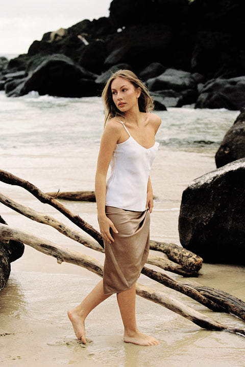 Model wearing white silk camisole and taupe silk slip skirt posing on the beach