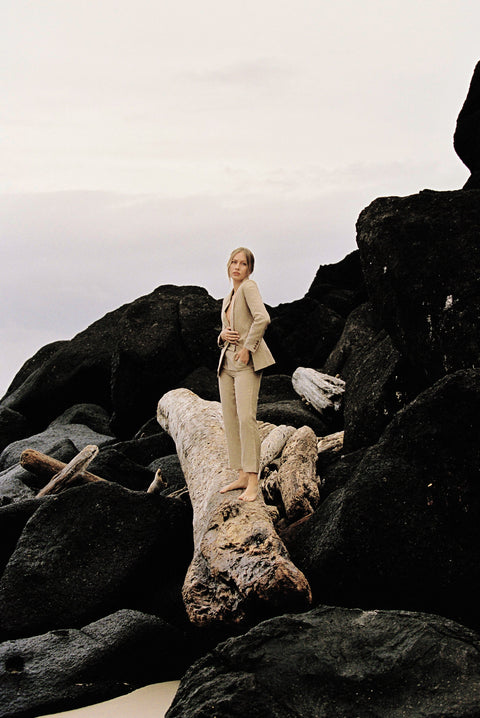 Model wearing a taupe linen blazer and trouser posing on a log by the beach